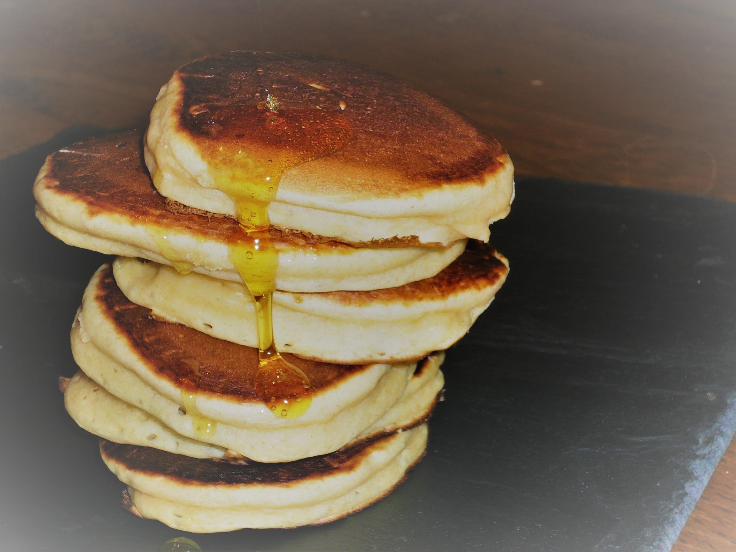 A stack of scotch pancakes with syrup trickling down them