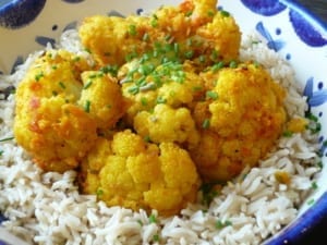 A bowl of cauliflower which has been baked with peppers, tomatoes and spices, served with rice