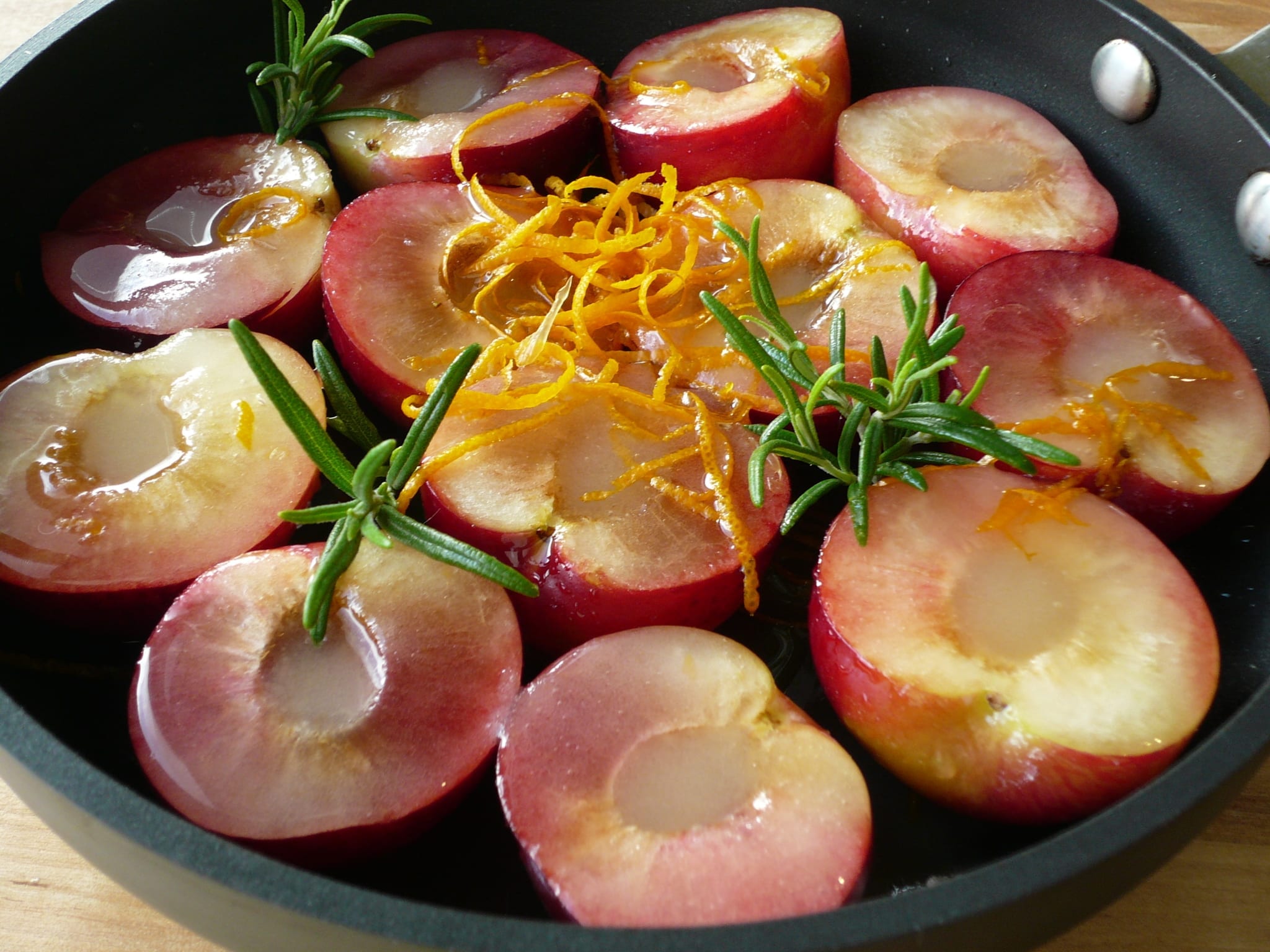 Halved & stoned plums sprinkled with sugar, orange rind & juice, studded with rosemary