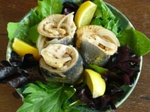 a dish of rollmop herring served on a bed of leaves with lemon wedges