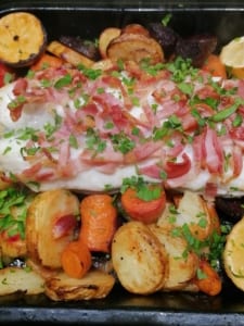 A tray of roasted vegetables topped with cod and crispy bacon.