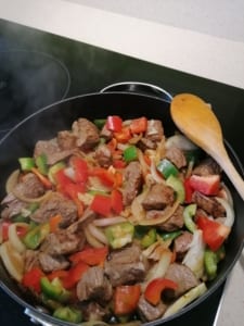 An image of beef cooking with red and green peppers
