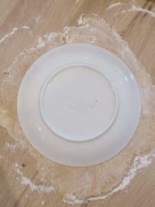An image of rolled pastry with an upturned plate used as a template