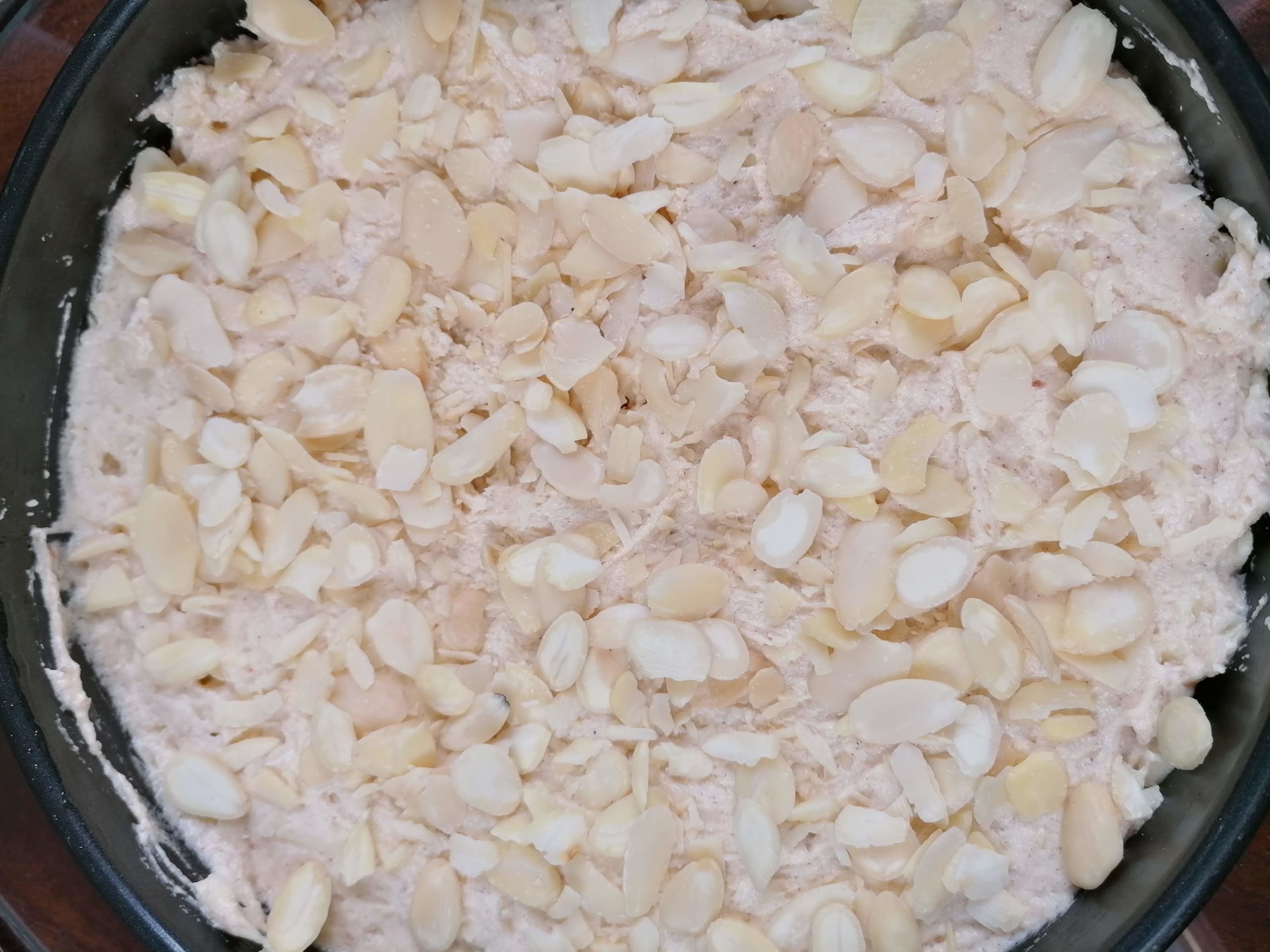 An image of the uncooked apple cake, sprinkled with flaked almonds ready for the oven.
