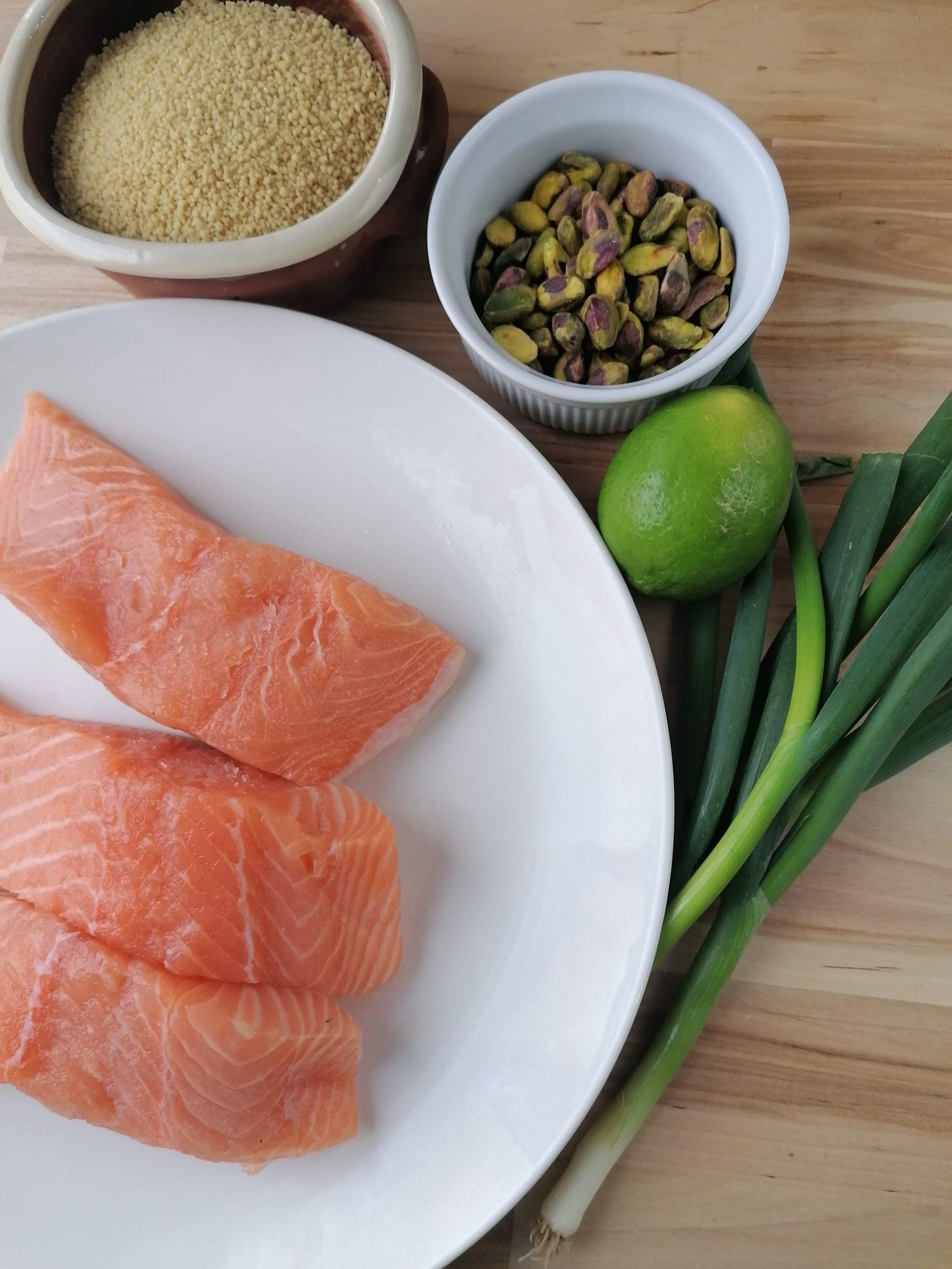 An image of salmon fillets, spring onions, pistachio nuts, couscous & lime