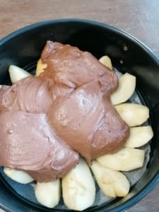 An image of chocolate cake mixture blobbed over pear quarters in a cake tin.