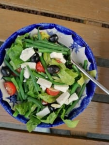 An image of a bowl of salad containing green beans, feta cheese tomatoes and black olives